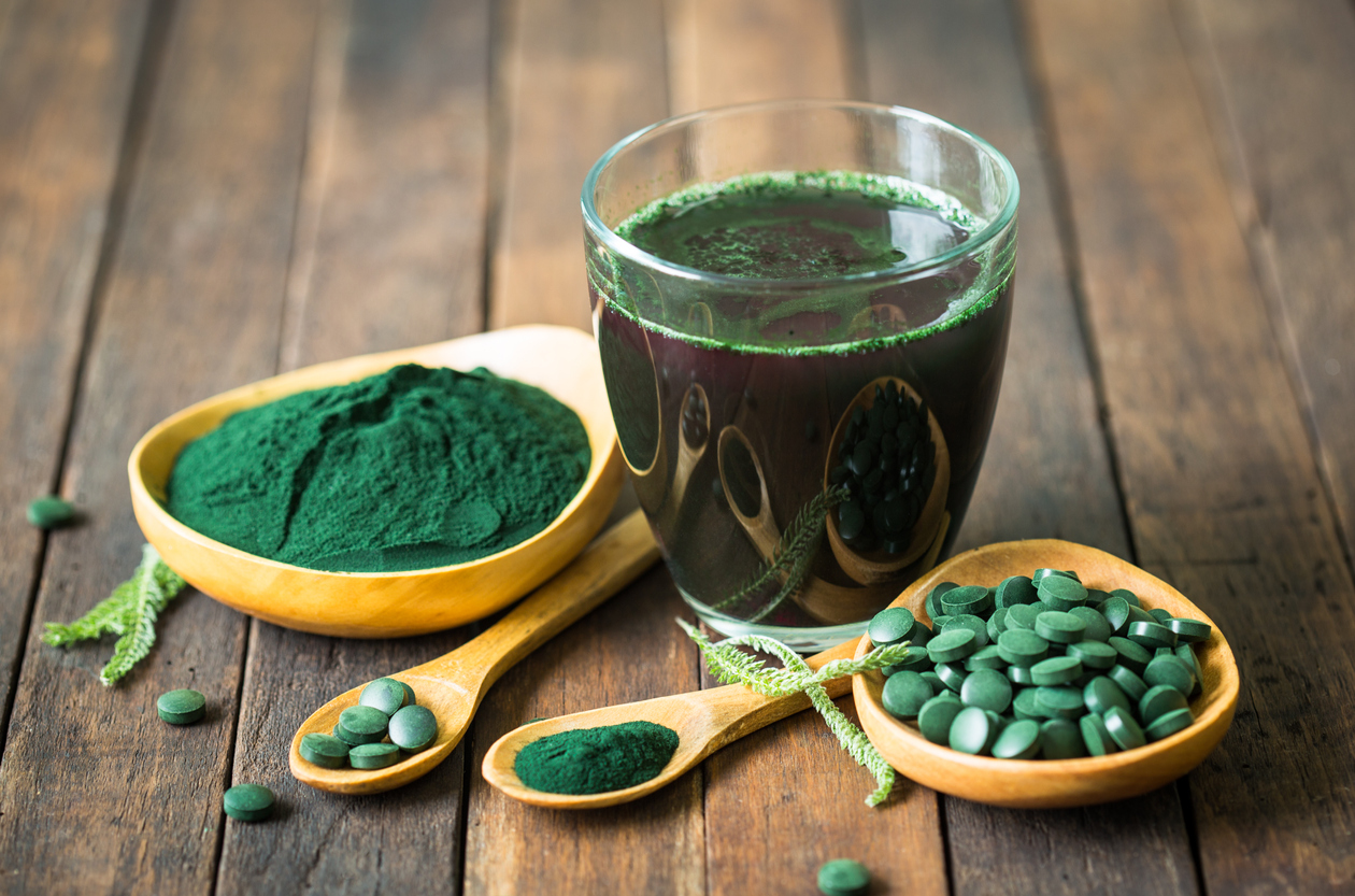 Chlorella juiced, bowl of chlorella tablets and spoonfuls of both chlorella tablets and powder on a wooden table