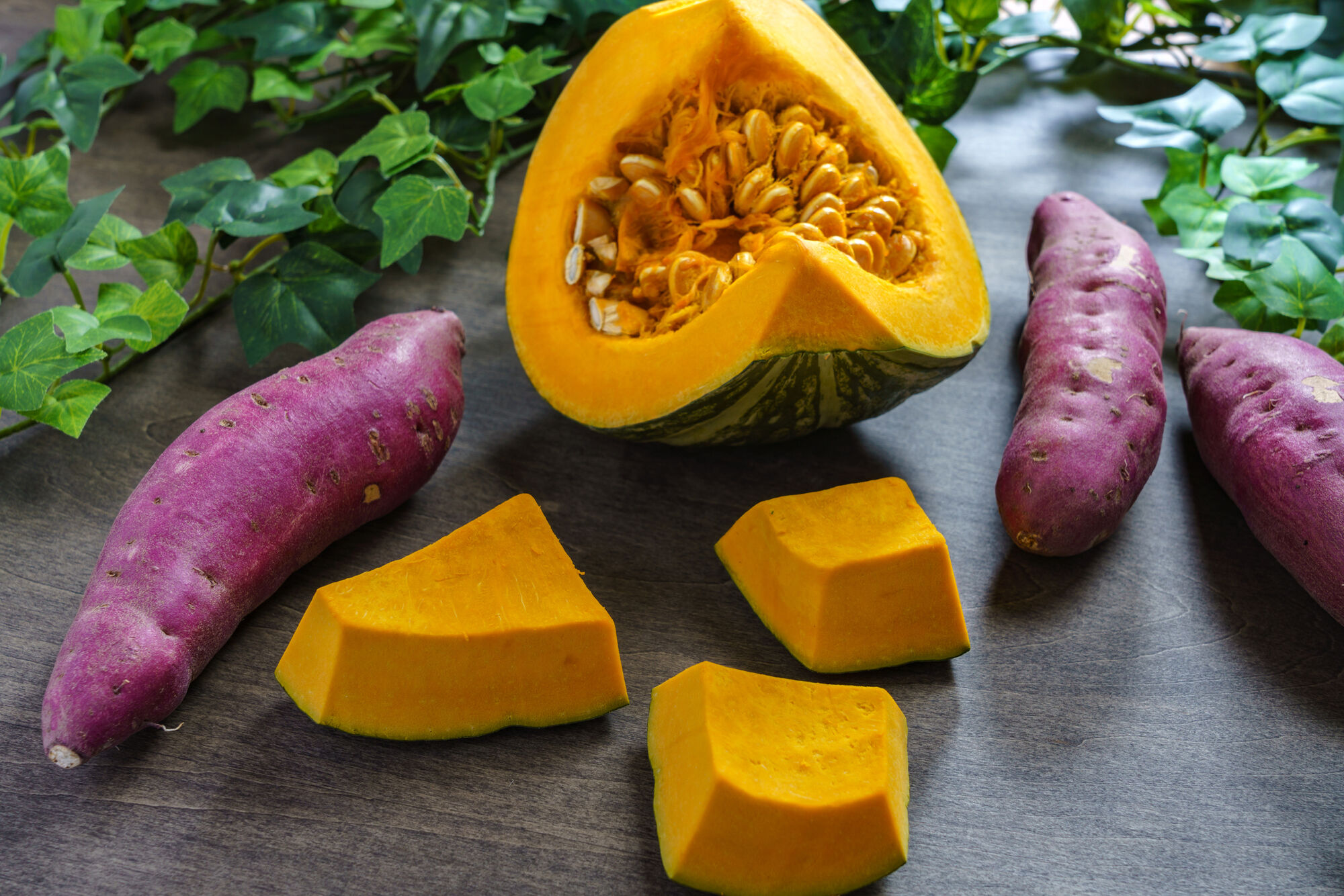 Cut up squash and whole purple sweet potatoes on a dark counter top