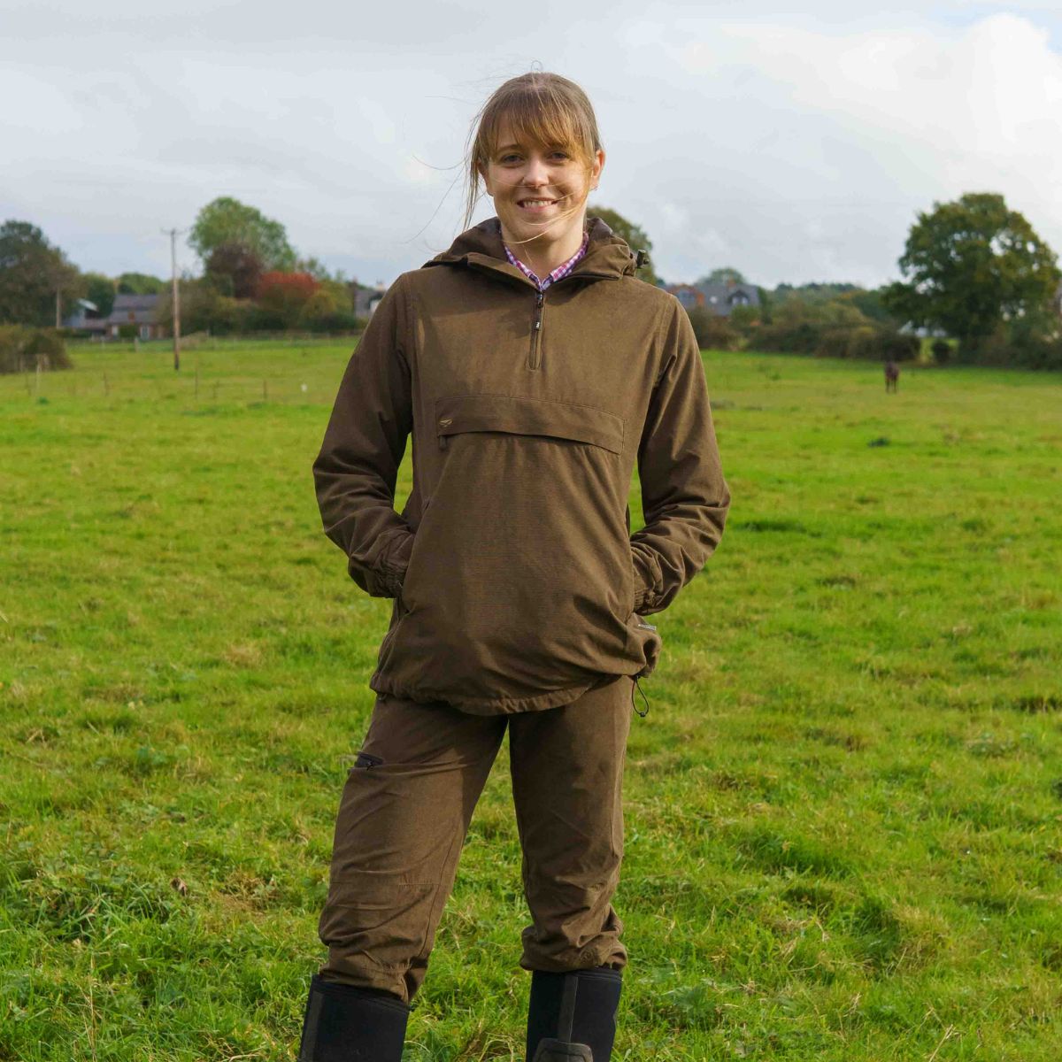 woman wearing a brown smock standing in a yard full of green grass