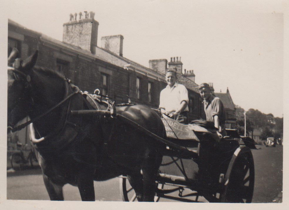 Black and white photo of 2 men delivering milk on a cart in 1960s.